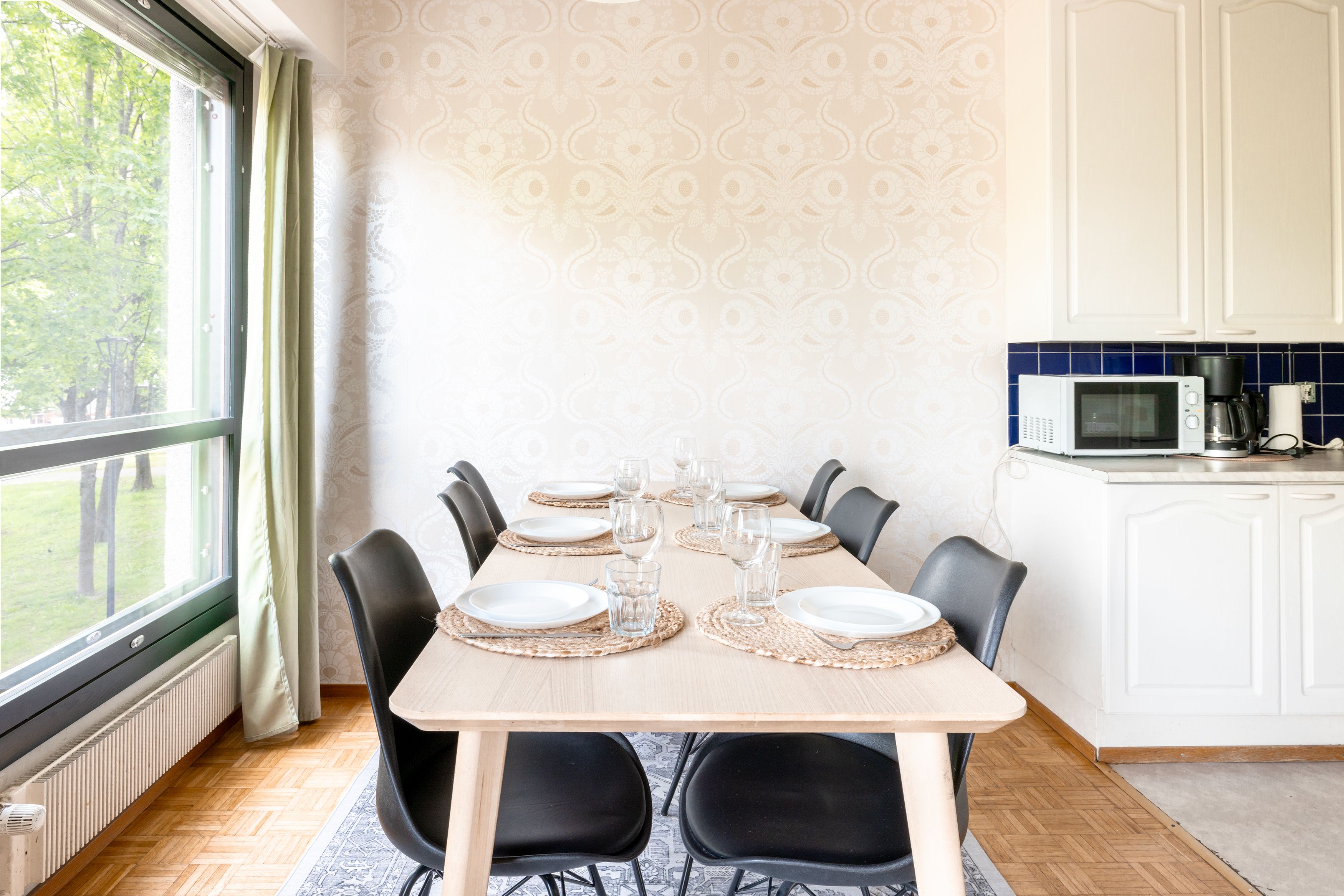 Comedor con una mesa dispuesta para seis, sillas y vistas al exterior a través de un ventanal.