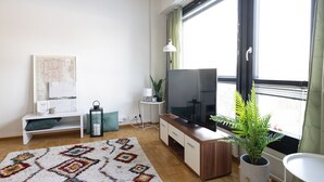 A modern living room with a large TV, a wooden cabinet, a patterned rug, and a potted plant. - Cozy 95m2 home With Sauna In Kaisaniemi (Helsinki)