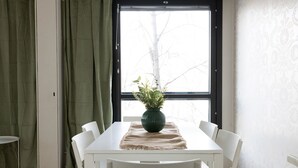 A dining area with a white table and chairs, a green vase with plants, and a window with a view of trees. - Cozy 95m2 home With Sauna In Kaisaniemi (Helsinki)