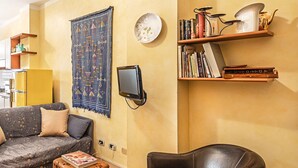 Een woonkamer met een bank, een leren fauteuil, een salontafel, een vloerkleed, een aan de muur bevestigde televisie en boekenkasten met boeken en decoratieve objecten.