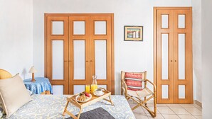 Een kamer met een bed, een houten stoel, een kleine tafel met een ontbijttafel, en twee houten deuren.