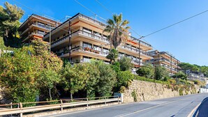 Un immeuble résidentiel à plusieurs étages, doté de balcons, d’un mur de soutènement en pierre et d’une végétation luxuriante.
