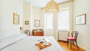 A neatly arranged bedroom with a bed, a wooden chair, a dresser, and a window with curtains. - Imperatrice Apartment by Wonderful Italy (Sanremo)