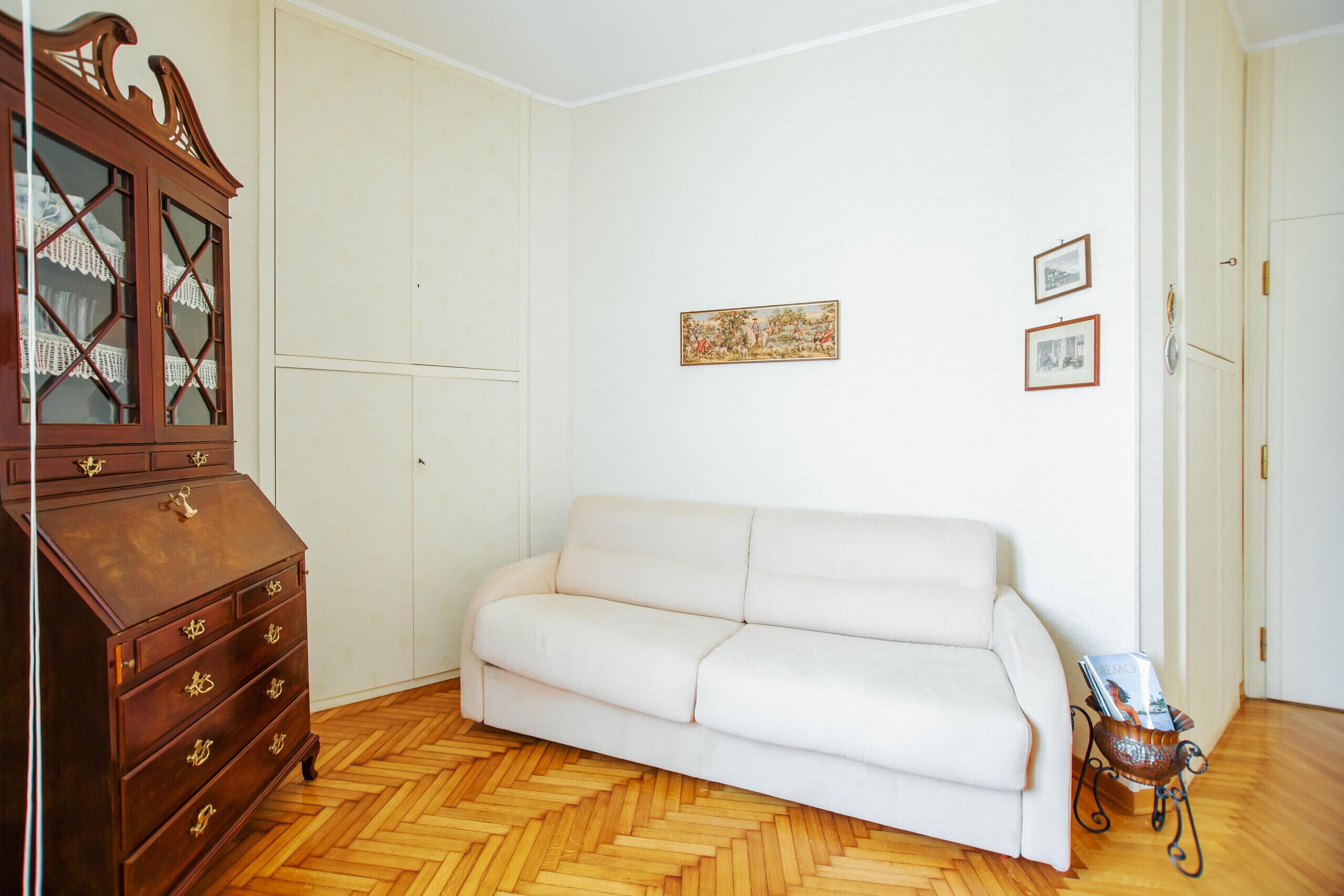 Een kamer met een witte bank, een houten dressoir en een houten vloer met een geblokt patroon.