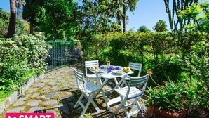 An outdoor patio with a table and chairs, surrounded by greenery and a stone pathway. - Imperatrice Apartment by Wonderful Italy (Sanremo)