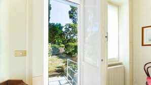 An open doorway to a balcony with a view of a garden, a radiator, and a chair. - Imperatrice Apartment by Wonderful Italy (Sanremo)