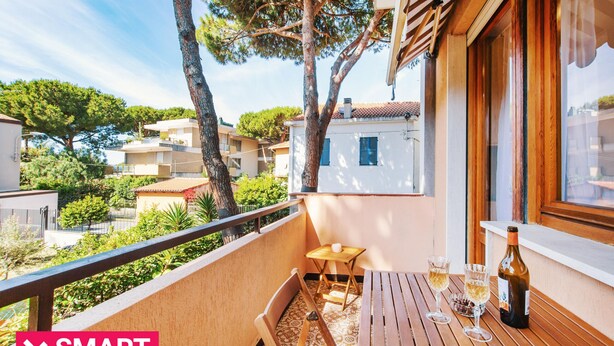 A balcony with a wooden table, two chairs, and a bottle of wine.