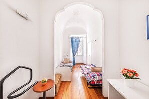 A narrow hallway with a bed, a small table with a plant, and a chair.