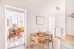 A dining area with a wooden table set for four, surrounded by chairs, a vase with flowers, and a framed picture on the wall.