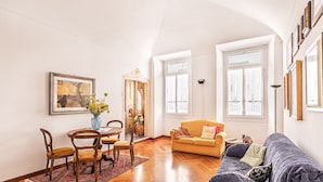 Ein Wohnzimmer mit einer Couch, einem Esstisch mit Stühlen und einer Vase mit Blumen.