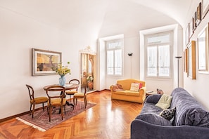A living room with a sofa, a dining table with chairs, and a vase with flowers.