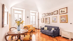 Ein Wohnzimmer mit einem Esstisch, zwei Sofas, einer Blumenvase und gerahmten Bildern an der Wand.