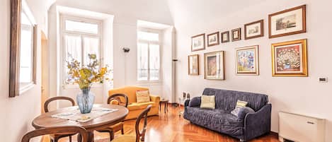 A living room with a dining table, two sofas, a vase with flowers, and framed pictures on the wall.