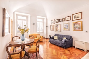 A living room with a dining table, two sofas, a vase with flowers, and framed pictures on the wall.