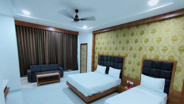 A hotel room with two beds, a sofa, a ceiling fan, and a patterned wallpaper.