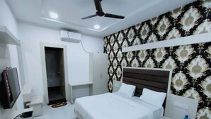 A modern bedroom with a large bed, a ceiling fan, an air conditioning unit, a wardrobe, and a television.