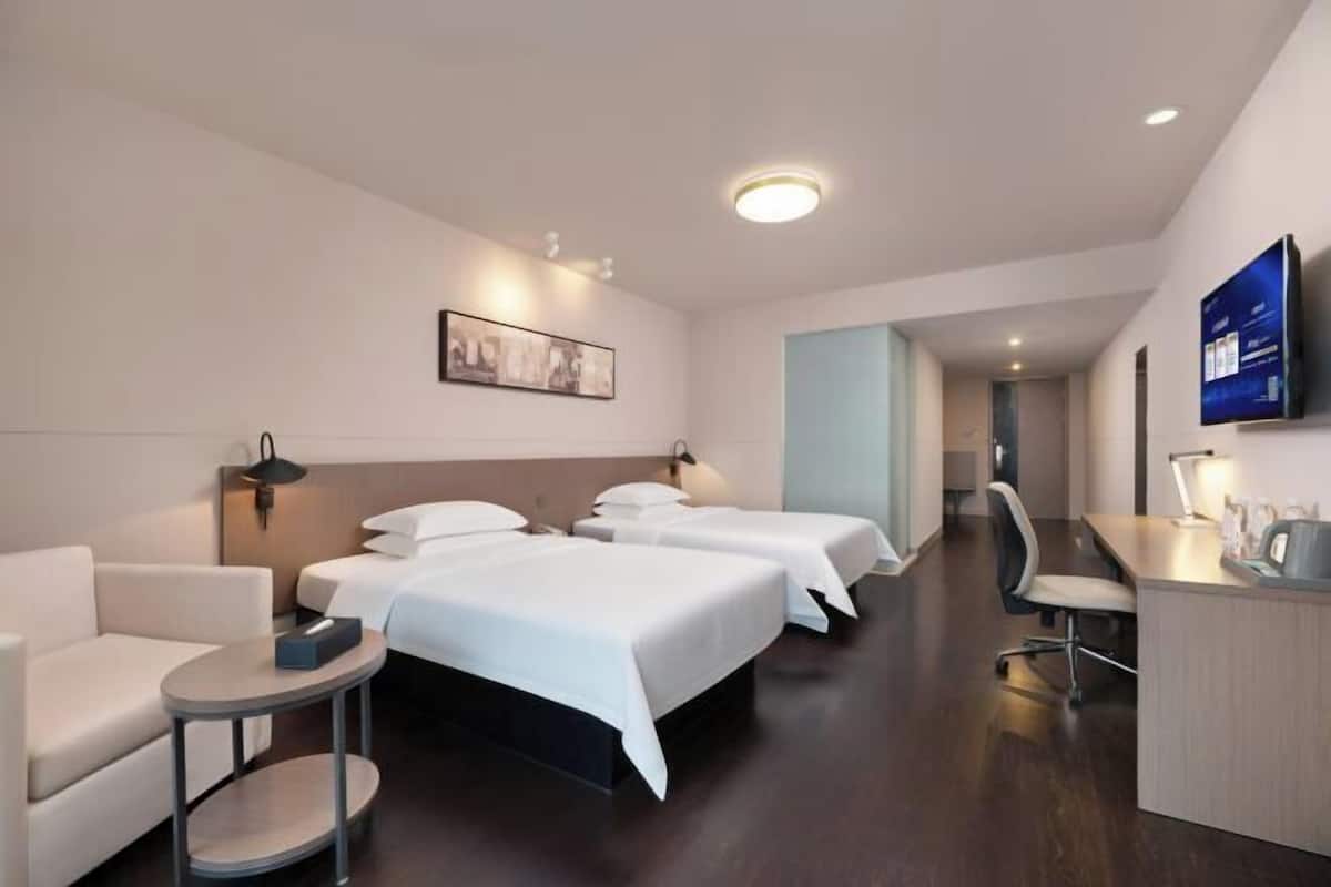 Habitació d'hotel amb tres llits, un escriptori, una cadira, una taula petita i un televisor fixat a la paret.