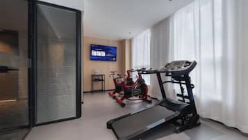 Habitación de hotel con una cinta de correr, un escritorio pequeño y un televisor de pared.