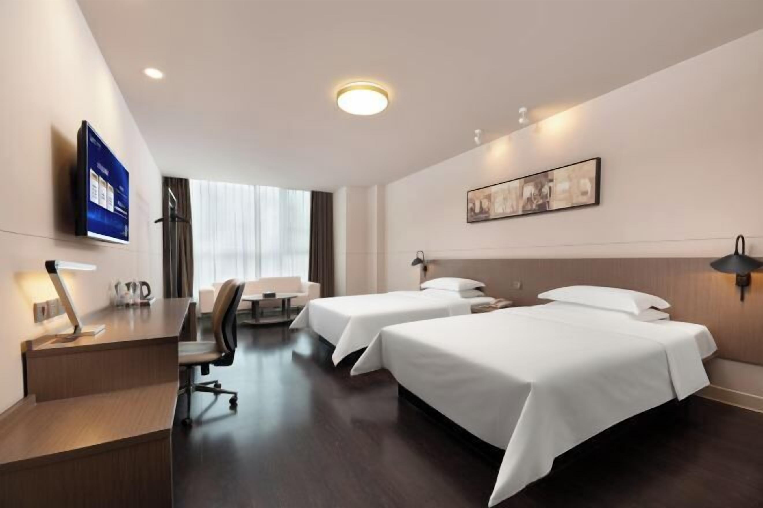 A hotel room with two beds, a desk, a chair, a flat-screen TV, and a painting on the wall.