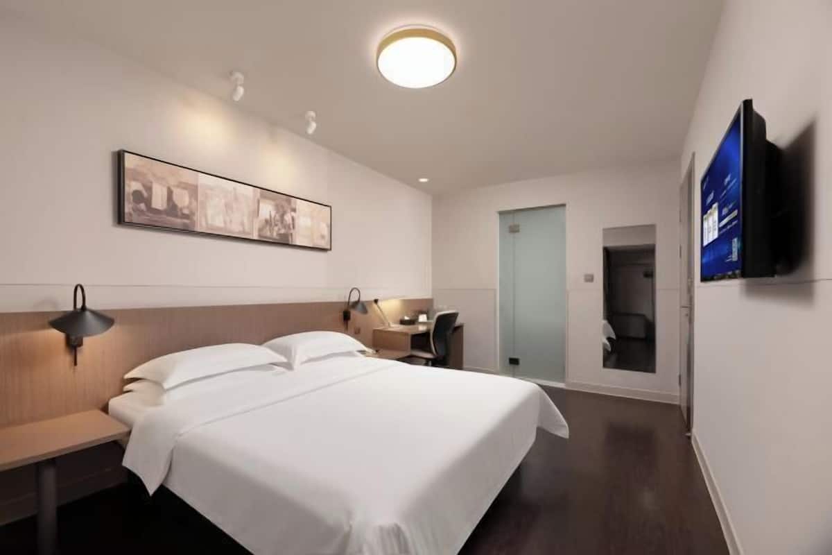 Habitació d'hotel amb un llit gran, taules de nit, escriptori, cadira, televisió de pantalla plana i un quadre al mur.