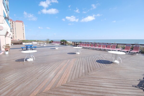 A wooden deck with tables and chairs, overlooking a body of water.