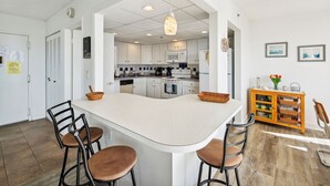 Een moderne keuken met witte kastjes, een centraal eiland met krukken, en een houten servieskast met manden.