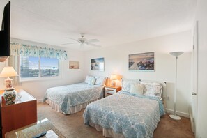 Une chambre avec deux lits, un ventilateur de plafond, une fenêtre donnant sur un beau paysage et une lampe.