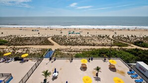 Een uitzicht op het strand met een terras met ligbedden en parasols.