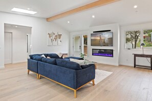A modern living room with a blue sofa, a flat-screen TV, and a fireplace. - Pacific Jewel: Brand New Build with Views (Monterey)