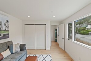 A hallway with a sofa, a rug, a clock, and a view of the outside.