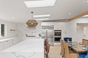 Een moderne keuken met een marmeren kookeiland, inbouwapparatuur en een eethoek met een hoge tafel en stoelen.