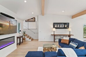 A modern living room with a flat-screen TV, a staircase, a coffee table, and a sofa.