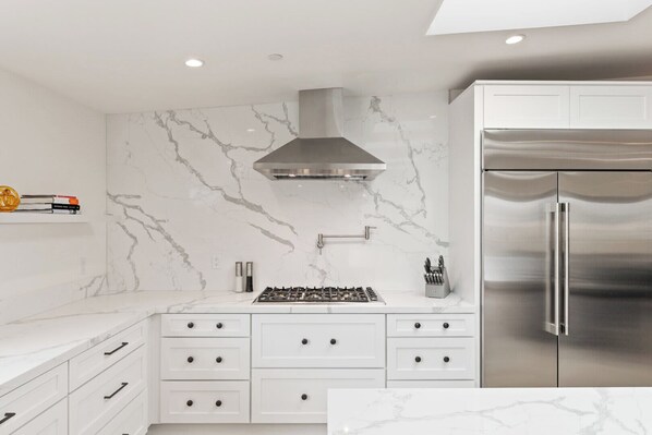 Een moderne keuken met witte kasten, een roestvrijstalen afzuigkap en een koelkast.