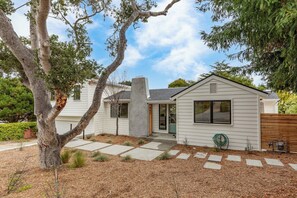 A modern single-story house with a front porch, a garage, and a well-maintained yard with mulch and stepping stones. - Pacific Jewel: Brand New Build with Views (Monterey)