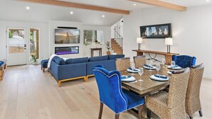 A modern living room with a sofa, dining table set for four, and a staircase leading to an upper level. - Pacific Jewel: Brand New Build with Views (Monterey)