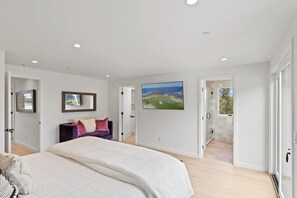 A bedroom with a large bed, a sofa, a painting, and a view of the outdoors.
