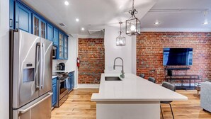 A modern kitchen with blue cabinets, stainless steel appliances, a brick accent wall, and a central island. - Elegant 2BR condo 3 blocks to French Quarter. King suite, garage parking, walk to Bourbon. (New Orleans)