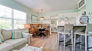 A modern kitchen with white cabinets, a microwave, and a dining area with a wooden table and chairs.