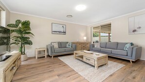 A modern living room with two grey sofas, a wooden coffee table, a large potted plant, and a framed picture on the wall. - Sea Renity - Coastal Hideaway (Bonny Hills)