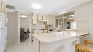A modern kitchen with a large island, white cabinets, and a dining area with a table and chairs. - Sea Renity - Coastal Hideaway (Bonny Hills)
