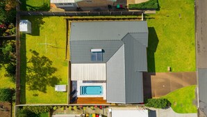 An aerial view of a house with a large garage, a swimming pool, and a well-maintained lawn. - Sea Renity - Coastal Hideaway (Bonny Hills)