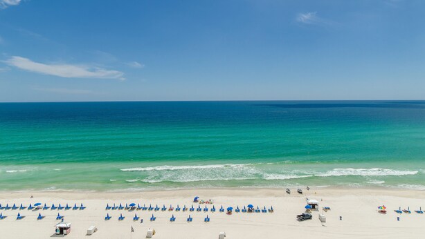 A beach with rows of blue umbrellas and a few beach chairs. - Beach Perfect Top of the Gulf 625-Beautiful Modern Beachfront Studio-Perfect Place in Paradise! (Panama City Beach)