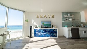 A modern kitchen with a large window overlooking the beach, a painting of a beach scene, and the word "BEACH" on the wall. - Beach Perfect Top of the Gulf 625-Beautiful Modern Beachfront Studio-Perfect Place in Paradise! (Panama City Beach)