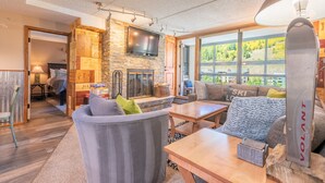 A cozy living room with a stone fireplace, a television mounted above it, and a large window offering a view of the outdoors. - Amazing condo next to the American Eagle lift.  Free WiFi, Free Parking (copper mountain)