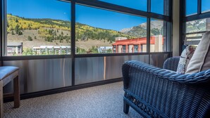 A balcony with a wicker sofa and a wooden chair, offering a view of a mountainous landscape and buildings. - Amazing condo next to the American Eagle lift.  Free WiFi, Free Parking (copper mountain)