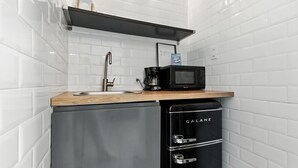 Een compacte keuken met witte betegelde muren, een roestvrijstalen spoelbak, een zwarte koffiezetapparaat, een magnetron, en een zwarte Galanz-koelkast.