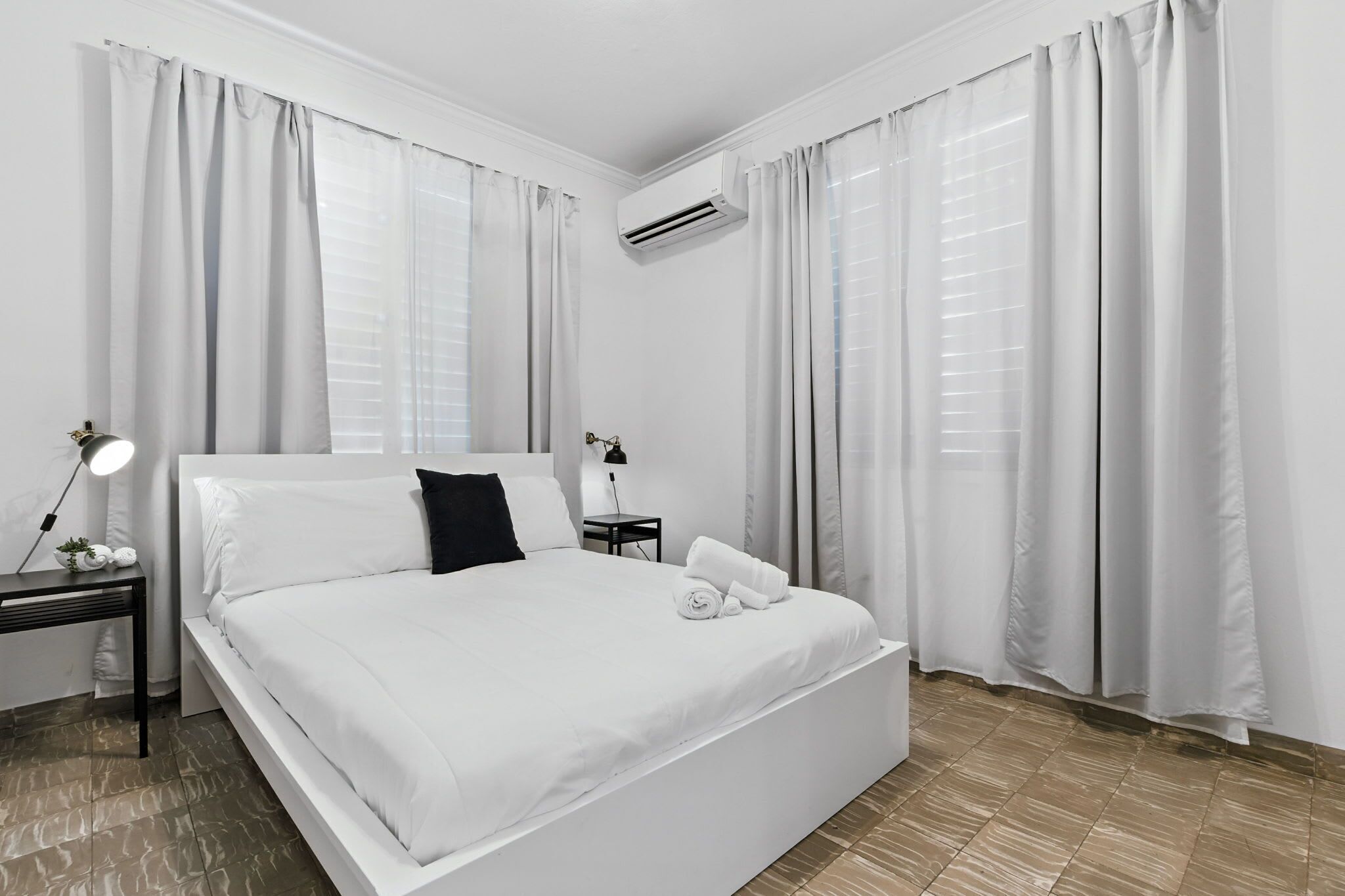A neatly made bed with white linens, a bedside lamp, and a small table with a lamp.