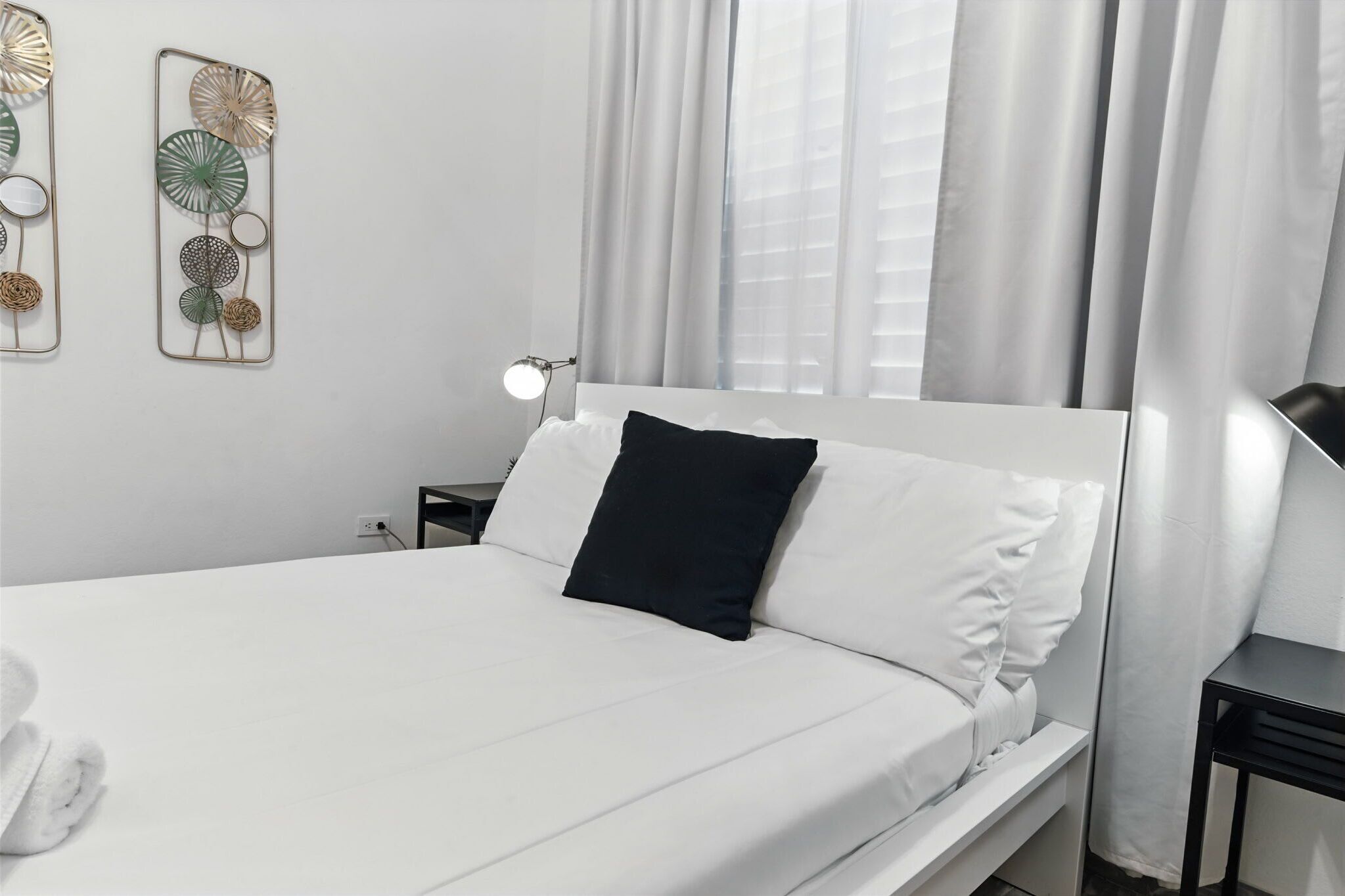 A neatly made bed with white linens, a black pillow, and a bedside lamp.