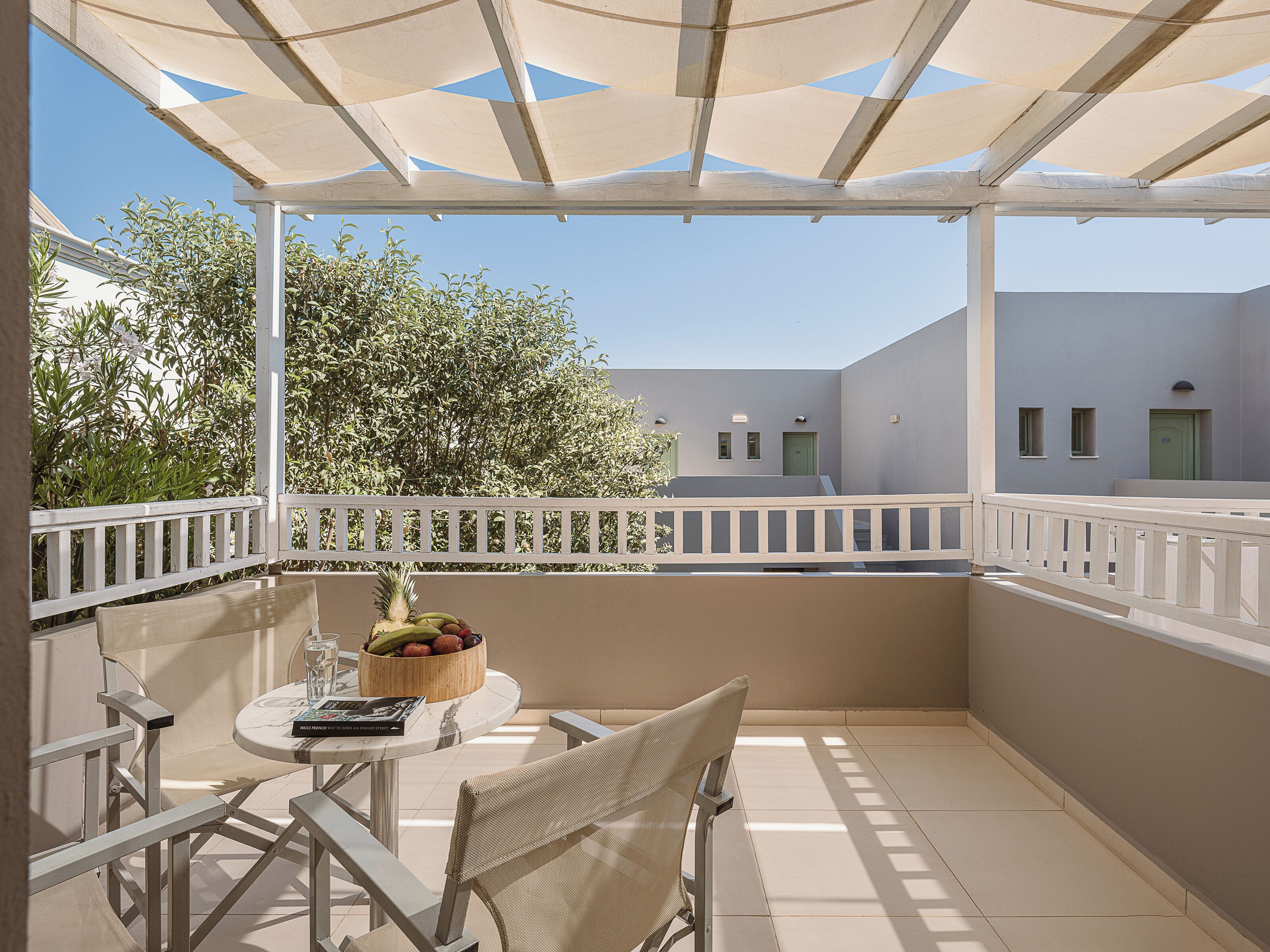 A balcony with a table, chairs, a fruit bowl, and a book.