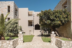 A stone pathway leading to a building with a balcony and a staircase.
